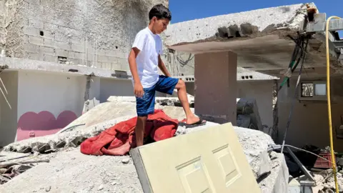 Lutfiyah al-Wahidi's grandson stands on pile of rubble