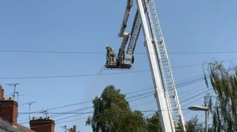 Leicester Media Online Fire crews using a hose from an elevated platform in a tree-lined street