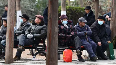 Getty Images A group of elderly people sitting on park benches, wearing winter coats