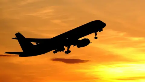 A plane in flight is cast is shadow. The sky behind it is bright orange and yellow as the sun sits low in the sky.