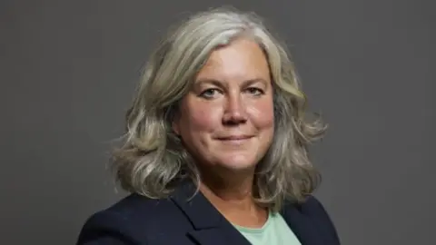 PA Transport Secretary Heidi Alexander wears a navy blazer and green top. She is smiling at the camera.
