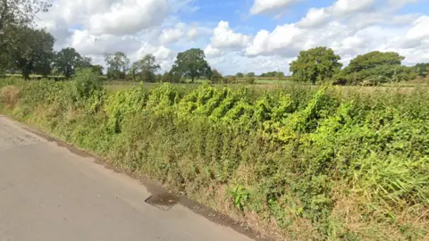 A Google street image is shown here of the Land at Fentonhouse Lane in Wheaton Aston set to have the new homes. There is a road, a car and a grass verge in the pictures. 
