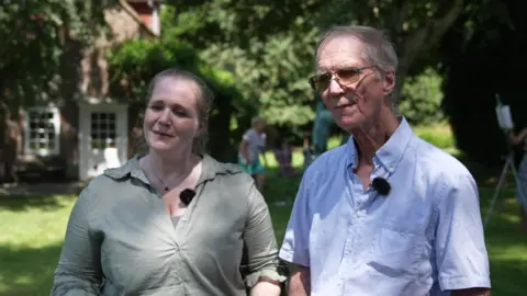 Sara Smith / BBC A man and a woman stood in a garden in front of a house.