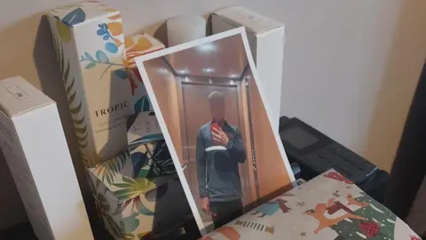 Essex Police A picture of a man wearing a navy and black Nike tracksuit. He has taken the picture with a red phone aimed at a mirror. The picture is on a cabinet, leaning on beauty products.