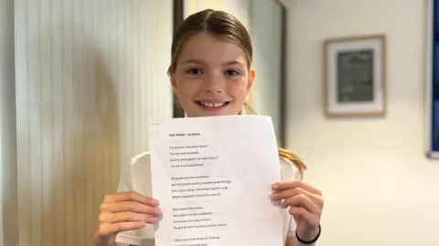 Matt Mackay/BBC A girl holds up a sheet of paper with a poem on it.