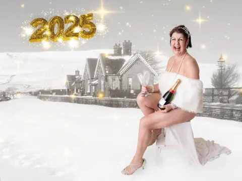 Nikita Kayleigh Photography A woman with short brown hair holding a bottle of champagne and wearing a pearl necklace sitting down along a train track covered in snow. She is draped in a white fur dress, which shows her legs. 