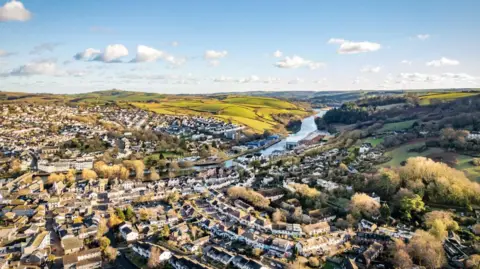 An aerial view of Totnes looking south with residential buildings nearest to the camera and fields and the River Dart in the distance