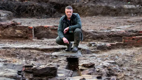 Malachy Conway, the National Trust's regional archaeologist for Northern Ireland, at the site of a complex of buildings dating back to the late 17th Century/early 18th Century that was discovered at Castle Ward, County Down.  Malachy has short, greying hair and is wearing a  dark green jacket and Wellington boots