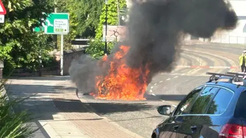 Fireball of orange flames coming from a car on a road
