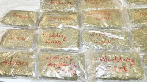 National Crime Agency  Cannabis in clear plastic bags laid out in rows. The packets have red writing on them, including some that say "wedding cake".