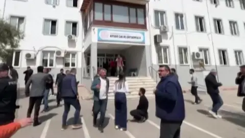 A grab of a video shows police, health workers and civilians outside a school were a shooting is reported to have taken place in southern Turkey