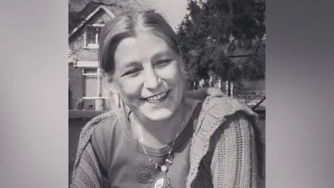 Handout Black and white image of Dawn Sturgess smiling. Her hair is tied back and she is wearing a loose cardigan.