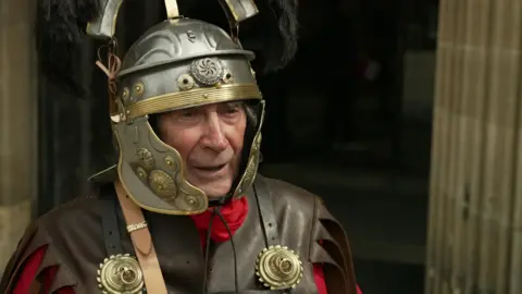 Martin wears a roman costume with a centurion's helmet.