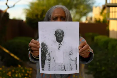 The Washington Post / Getty Images Carole Coles Henry holds a black and white photo of her great great grandfather Clem Coles as she stands in the backyard of her home in Phoenix, Arizona, US on 11 November 2022 in Phoenix, Arizona. Clem Coles was enslaved on the Coles Hill Plantation in Chatham, Virginia. 