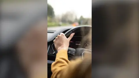 Rear seat view of woman in yellow jumper driving a car.