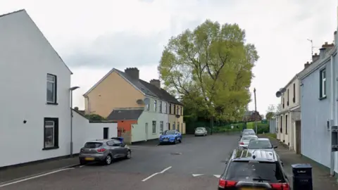 A generic Google street view of a terraced street during the day. Cars are parked along it. A tree can be seen.