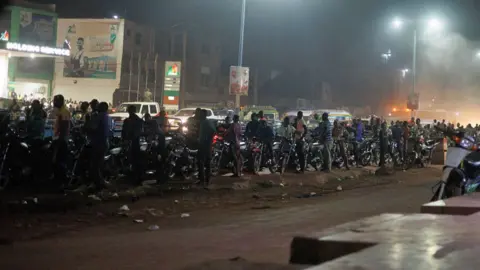 AFP/Getty Images Cars and motorbikes in a petrol queue at night at a service station in Bamako, Mali -  27 October 2025.