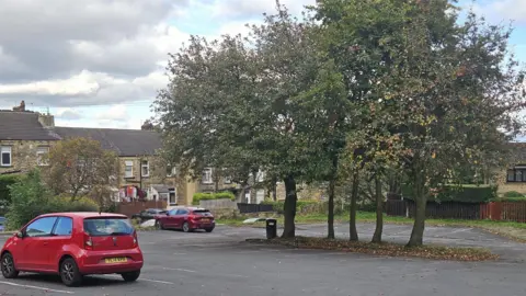 Aisha Iqbal/BBC A grey-tarmacced car park with just two small red cars parked in it.