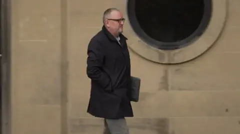 Paul Moore, a man with short grey hair, leaves court dressed in a black coat and grey trousers.