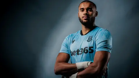 Gavin Bazunu poses in a Stoke goalkeeper top