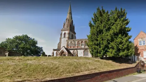 Google A large grey church sits behind a grass lawn with headstones.