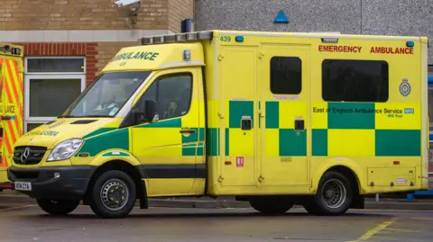 PA Media A yellow and green ambulance parked in a car park.