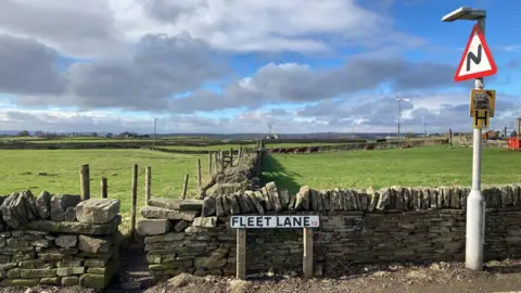 Dry stone walls and a footpath leading into green fields with a street sign reading Fleet Lane