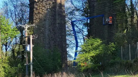 Emma Barrett Man in high vis and helmet on crane carrying out works on a stone viaduct 