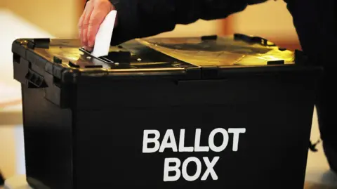 Black ballot box with white writing with hand putting polling card in to the box 