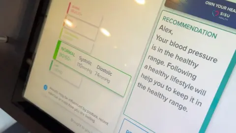 A close-up of the health check machine screen, with a normal rating for heart rate showing on the left and on the right a "recommendation" that says blood pressure is in the healthy range.