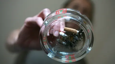 Alamy Smoker extinguishes a cigarette into a used ashtray on top of a glass coffee table