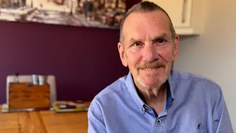 Man in blue shirt sits at dining table.