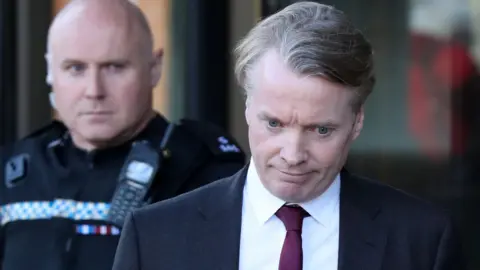 PA Media Craig Whyte, a middle aged man with sandy hair, outside court. He is looking down, while wearing a black blazer, a white shirt and a purple tie.