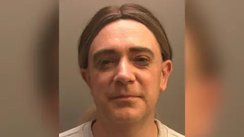 A police head and shoulders photo of Katie Birtles with long brown hair tied back into a ponytail, looking directly into the camera.