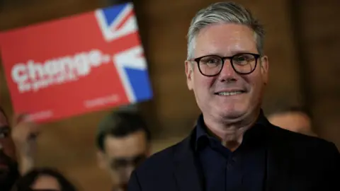 Reuters Sir Keir Starmer pictured smiling at a campaign event with a blurred Labour banner saying 'change' in the background 