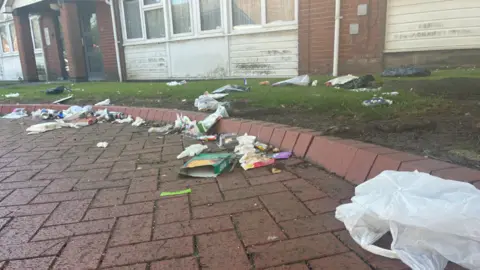 Local Democracy Reporting Service Lots of rubbish on a brick-patterned floor outside a block of flats.