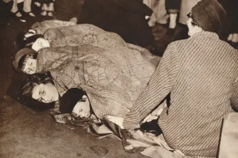 Getty Images A mother watches over her children as they sleep on The Mall, to ensure their place to see the coronation of King George VI