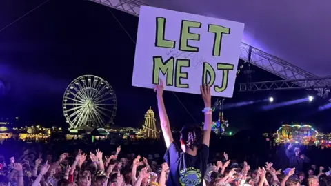 Frost Family Harry Frost holding up 'let me DJ' sign in front of a crowd