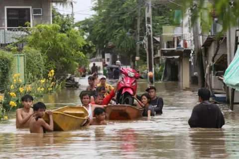 EARVIN PERIAS/AFP Residents transport a motorcycle on a boat to avoid floodwaters left by torrential rains of Typhoon Doksuri in Calumpit, Bulacan province on July 29, 2023.