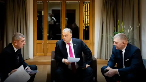 Viktor Orban/X Three men sit in a room in their suits, with one man in a red tie in the centre