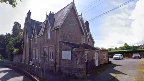 Google A google maps image of a care home. It is a large brown brick building with a car park to the right hand side. It has a pointed roof