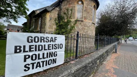 A sign which says polling station, hanging from a black gate outside a church