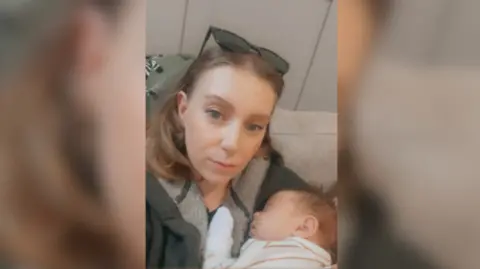Supplied The photo is a selfie of a woman with blonde hair and sunglasses on her head. She is holding a sleeping baby. 