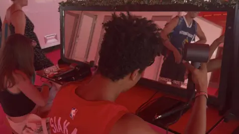 George King/BBC A young man drying his hair in front of a mirror. 