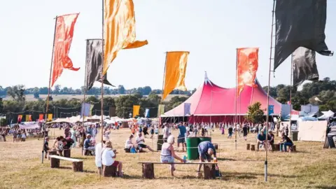 PA Media Revellers attend the Black Deer Festival in a field on a sunny day with tents in the background 