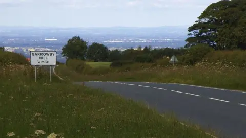 Geograph A view of the A166 from the top of Garrowby Hull in East Yorkshire. The road is surrounded by grass verges and fields and trees are visible in the background.