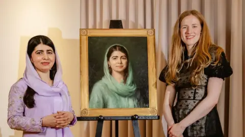 Lady Margaret Hall Malala Yousafzai is wearing a lilac dress and headscarf and is standing next to the new painting of her, as well as its artist Isabella Watling.