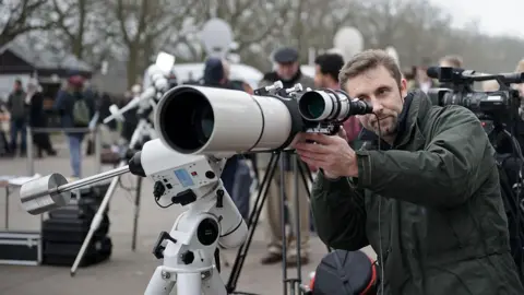 Getty Images Man looks through a telescope during a public solar eclipse viewing event in London.