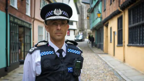 Norfolk Police A portrait photo of Chief Constable Paul Sanford standing in a street and wearing his uniform