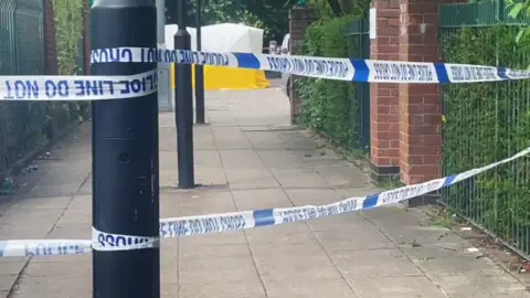A police forensics tent can be seen behind police tape